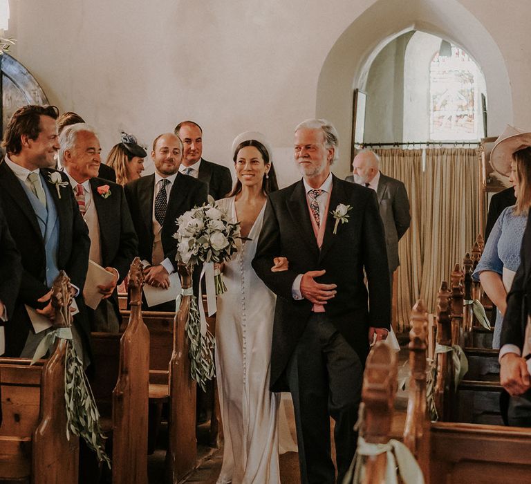 Bride in a satin button Ghost wedding dress and chunky headband is walked down the aisle by the bride's father 