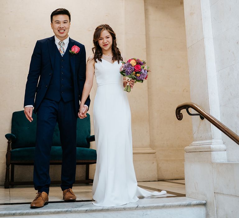 Bride wears elegant and classic white wedding dress whilst holding brightly coloured floral bouquet 