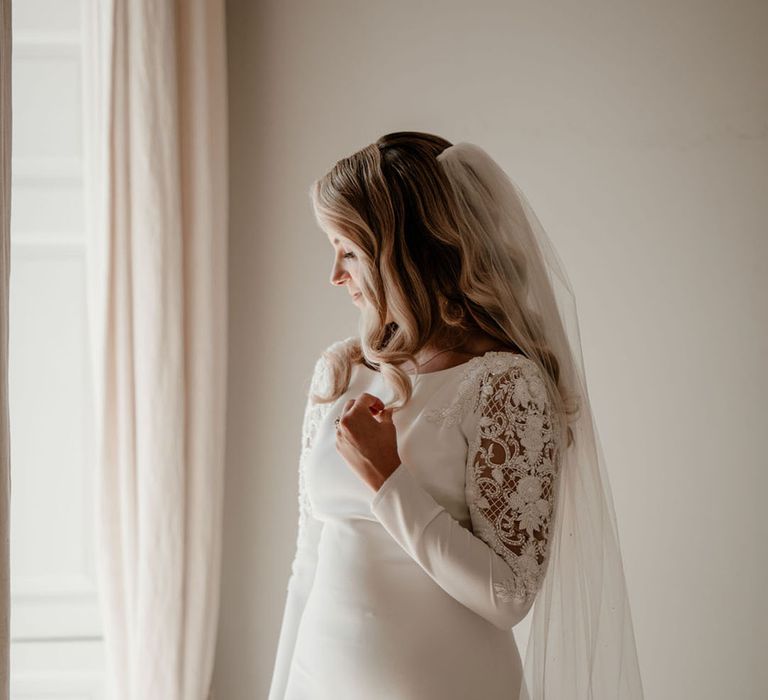 Bride in a long sleeve fitted wedding dress with intricate lace and beading on the sleeves and a veil 