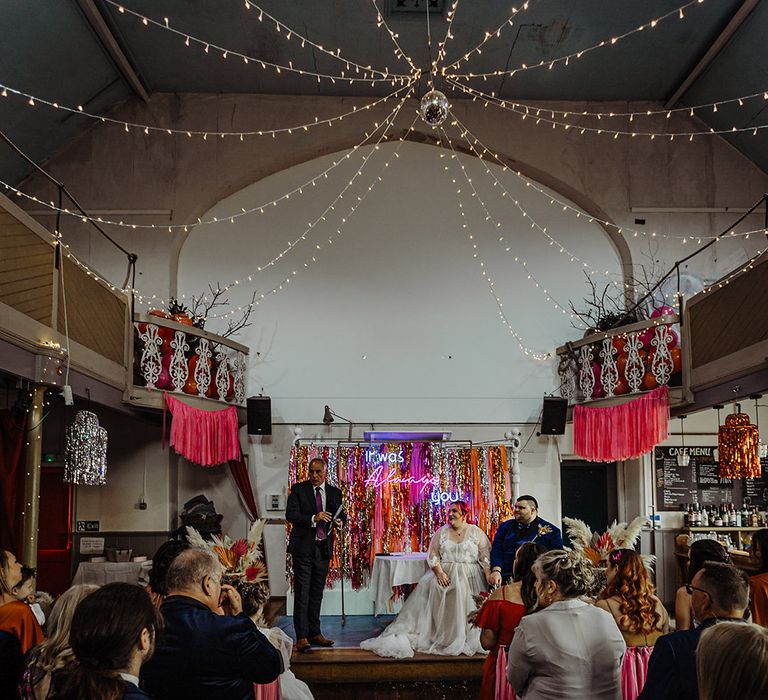 Zion wedding venue with pink, orange, red, silver and gold metallic streamer backdrop, pink streamers on the backs of chairs, gold and silver streamers hung on the lights, and fairy lights and disco ball decorations hung on the ceiling