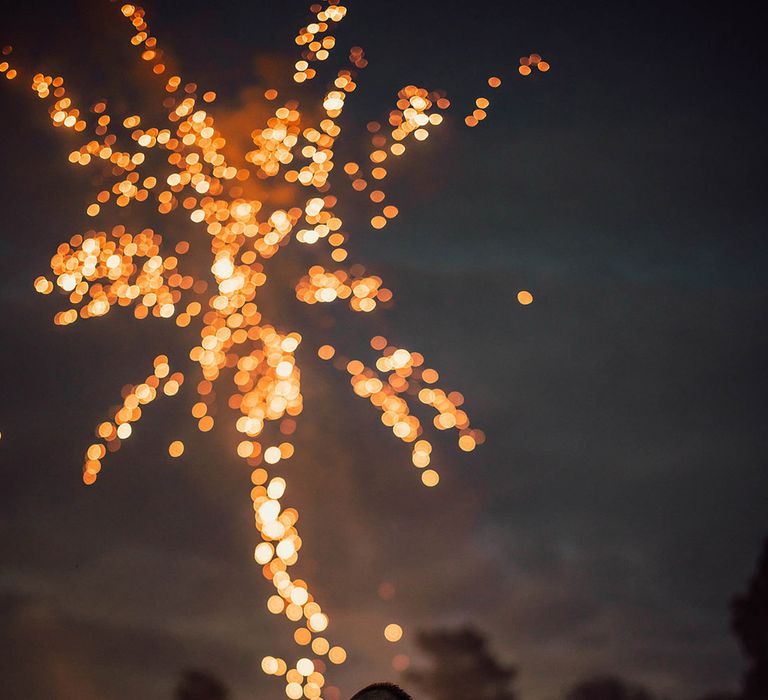 Bride and groom share a kiss as fireworks go off in the background 