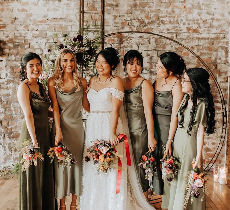 Bride in off the shoulder lace wedding dress with bridesmaids in olive green satin bridesmaid dresses 