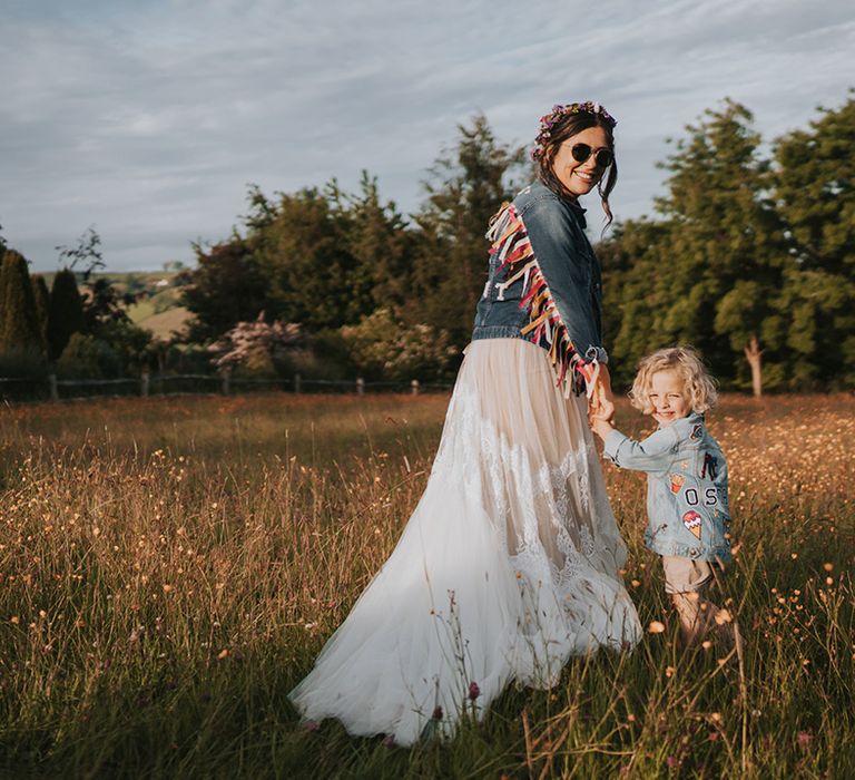 Bride in personalised denim jacket walks through fields with her son wearing personalised denim jacket 