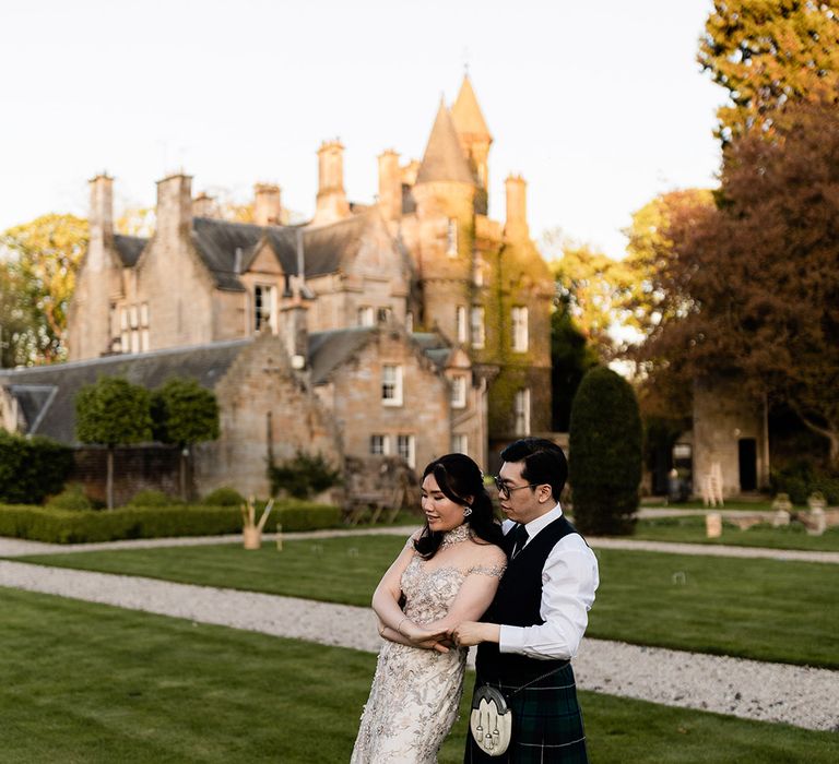 Bride wears embellished bespoke reception dress as her groom embraces her outdoors during golden hour