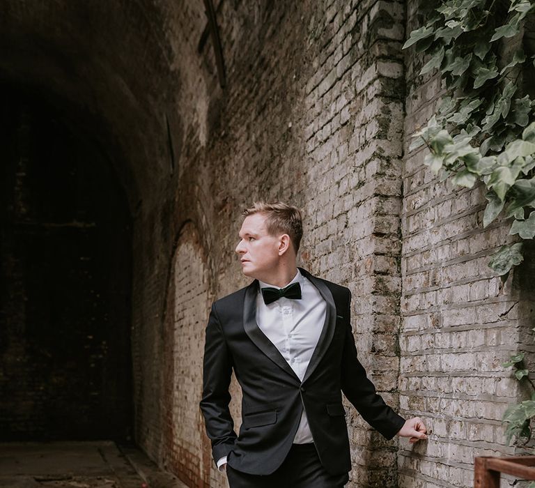 Groom in stylish black tuxedo with black bowtie with light orange rose boutonniere at multicultural Christmas wedding with Lion Dance