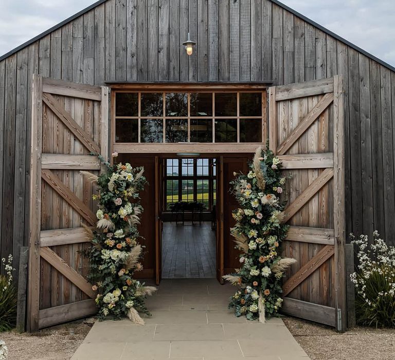 Rustic barn wedding with two flower columns decorating the entrance with pampas grass and roses