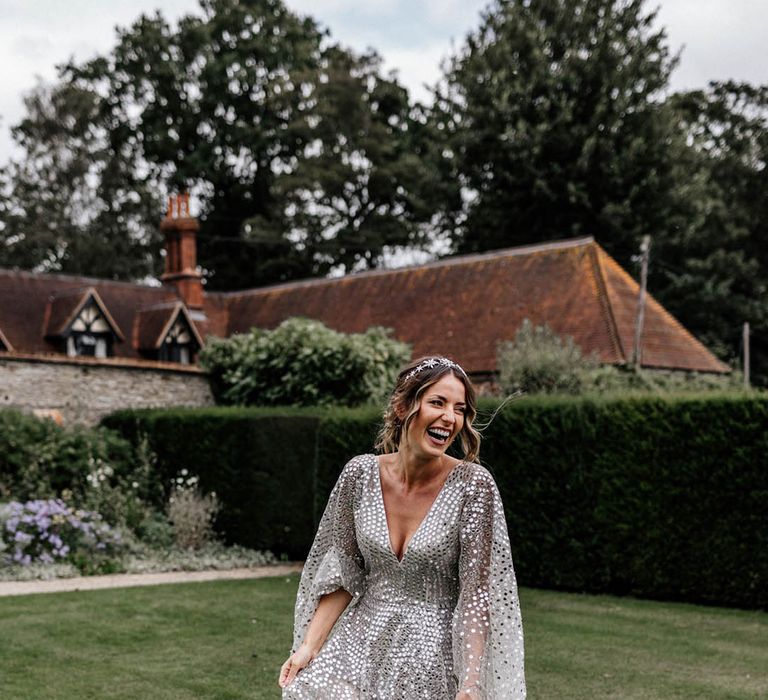 Bride wears silver sequin wedding dress with long sheer full sleeves and bridal crown whilst holding colourful floral bouquet 