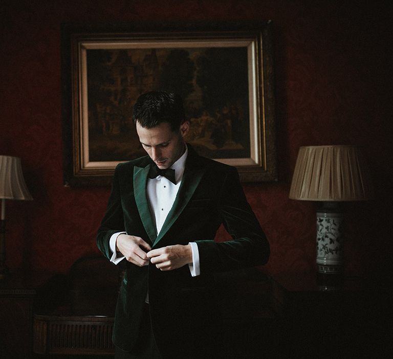 The groom in a velvet green tuxedo with a black bow tie gets ready for the wedding 