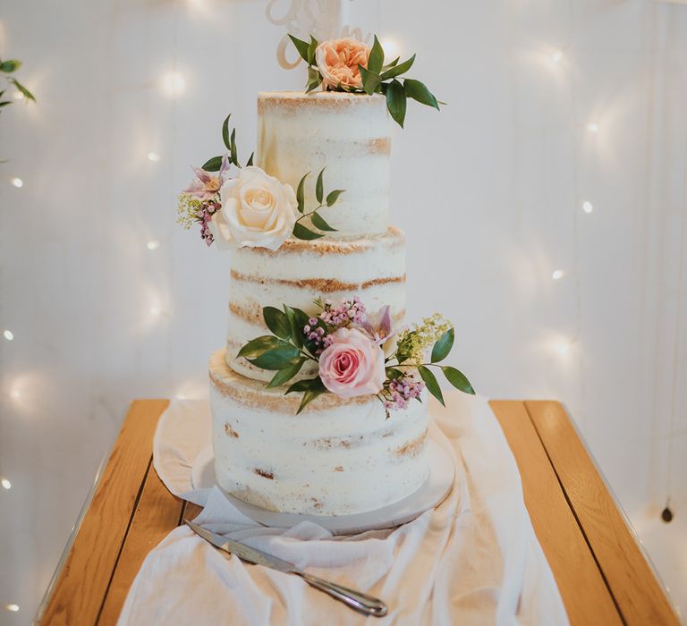 Rustic three tier semi-naked wedding cake with white icing with pastel roses and custom white cake topper 