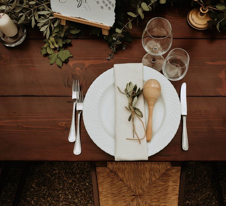 Wooden table setting with white napkins, ecaluptus, candles and maraca favours