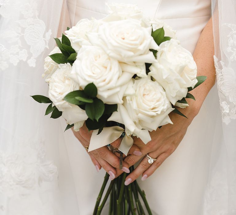 Classic white rose wedding bouquet with long stems worn by bride with rounded pink nails 