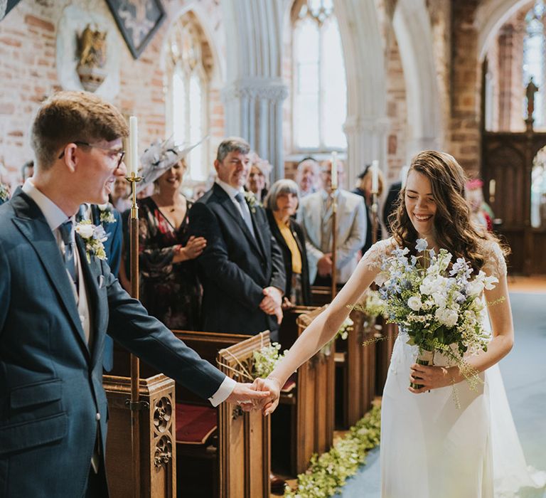 The bride reaches out to hold hands with the groom after walking down the aisle to him for the church wedding 