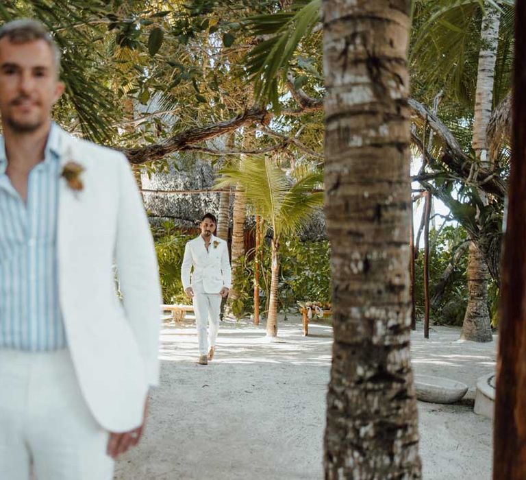  Groom wearing white blazer, light blue and white striped shirt, dusky orange garden rose and dried flower boutonniere, white suit trousers and gold jewellery doing first look photo with groom in white blazer with dusky orange garden rose and dried flower boutonniere, white shirt, white suit trousers 