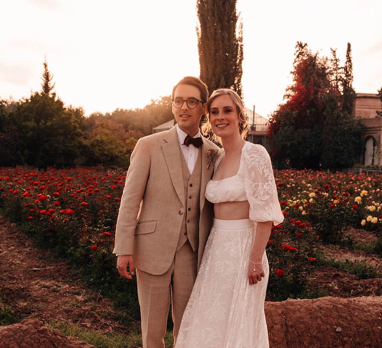 Groom in cream suit with red bow tie with the bride in bridal separates from Grace Loves Lace at Morocco wedding 