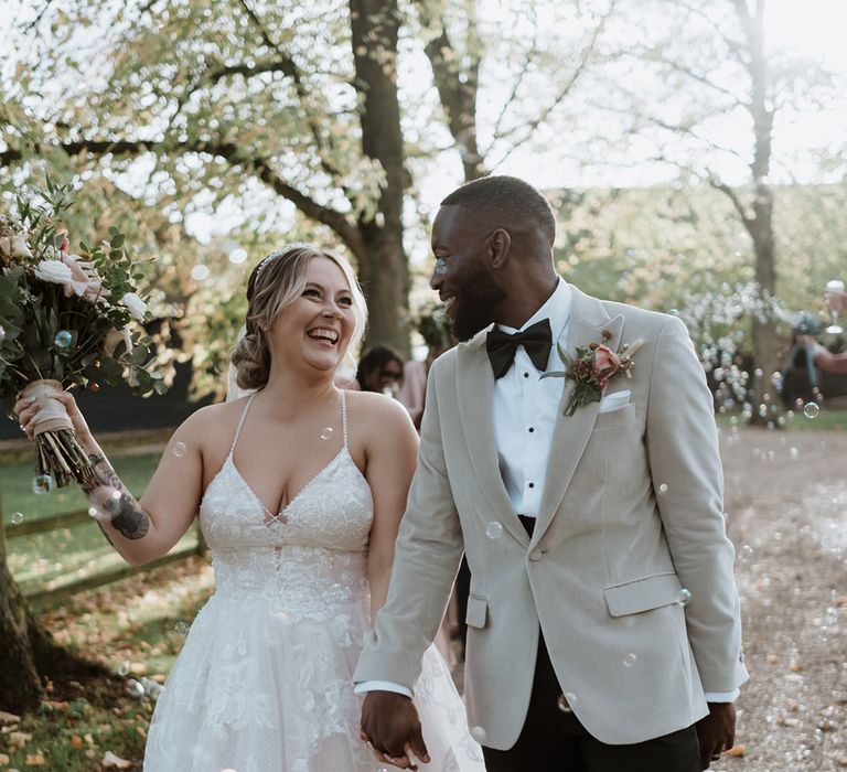 The bride and groom walk hand in hand as they exit their ceremony to bubbles 