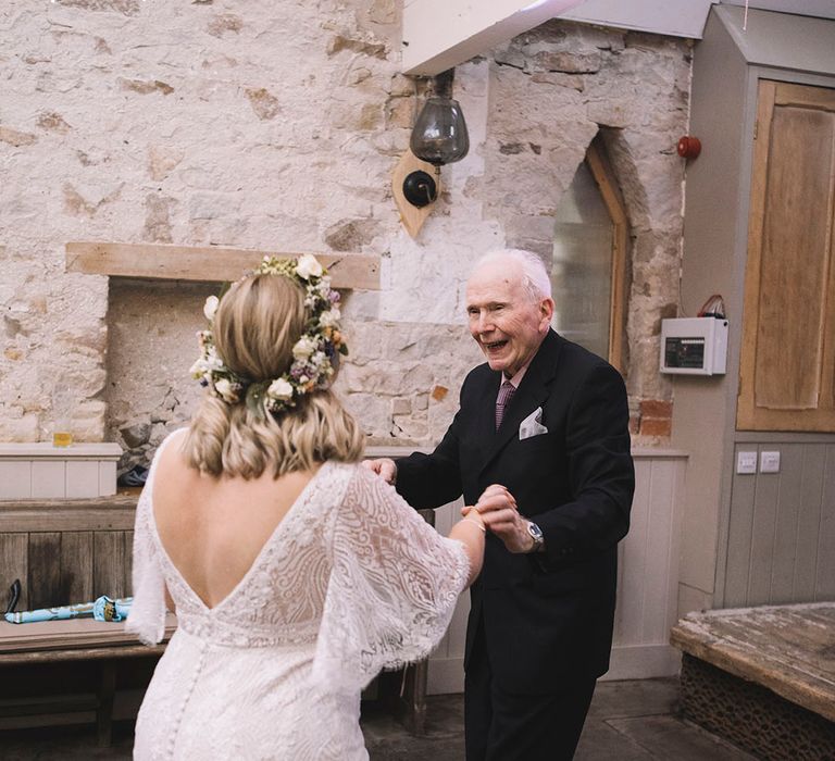 The bride in a boho lace wedding dress dances with her grandad on her wedding day 