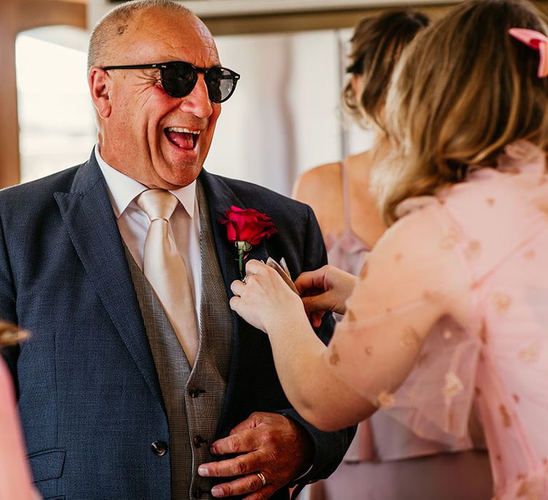 Father of the bride in navy suit with sunglasses and bright pink flower buttonhole 