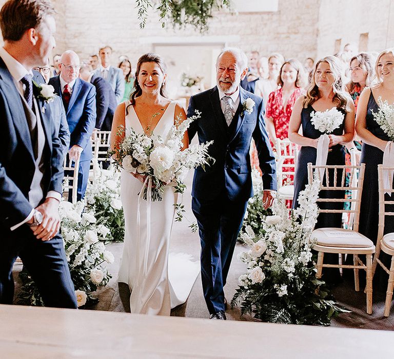 Father of the bride and bride walk down the aisle together with the groom waiting at the altar for the bride 