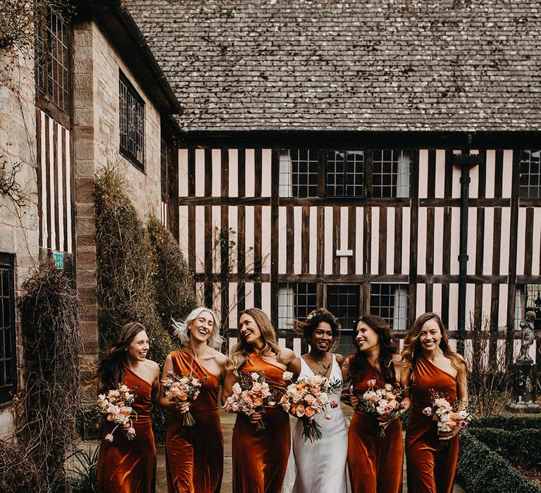 One shoulder orange velvet bridesmaid dresses worn by bridal party walking with the bride at Brinsop Court wedding 