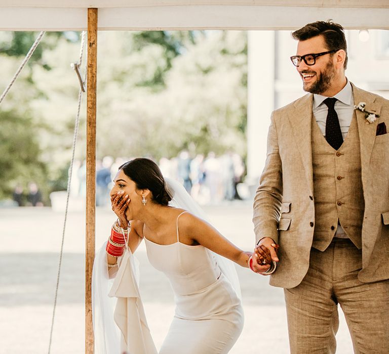 Bride in a fitted wedding dress reacting to the stunning marquee wedding decorations with the groom 