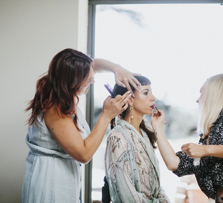 Bride in bridal robe having hair and makeup done featuring a dark red lip