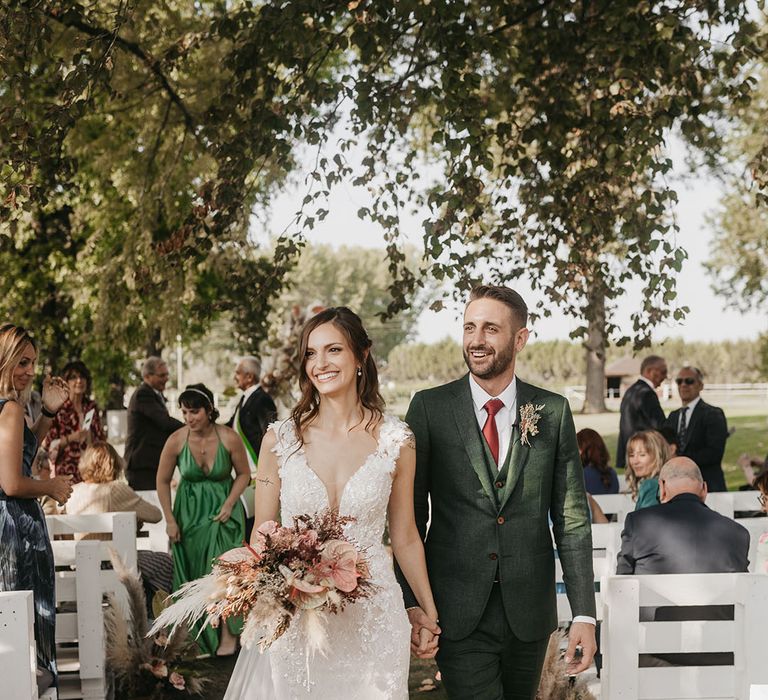 boho tenuta il cigno wedding ceremony with bride in an appliqué wedding dress and groom in a dark green suit descending up the aisle as husband and wife 