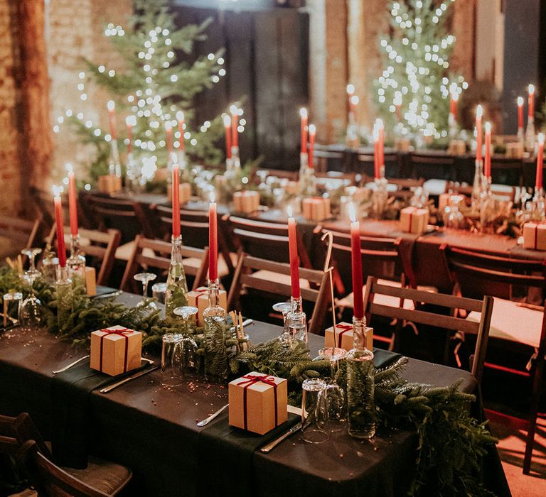 Evergreen foliage as table runners with red candles and present wedding favours 