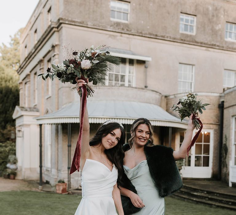 Maid of honour wearing a faux fur shawl over a green satin dress with the bride in an off the shoulder gown 