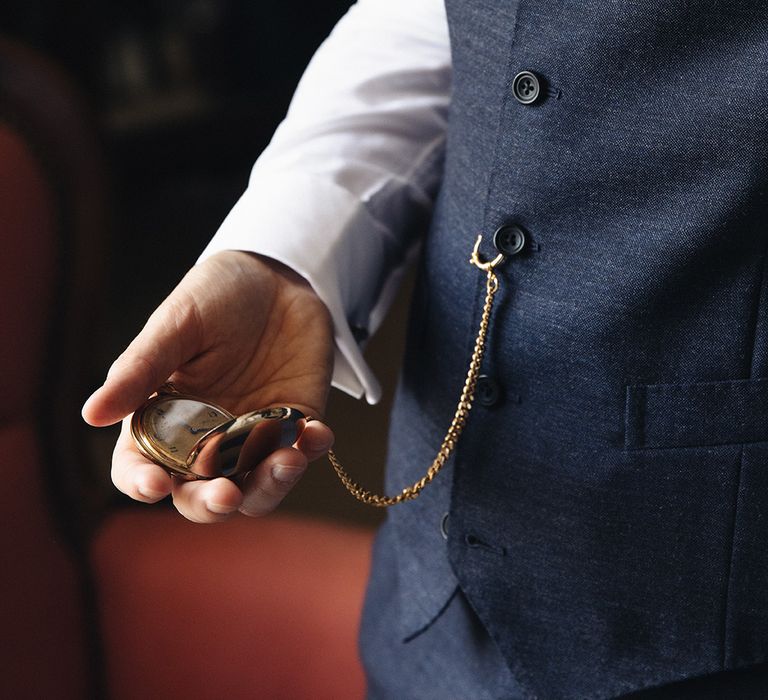 Groom in navy waistcoat holding gold pocket watch accessory 