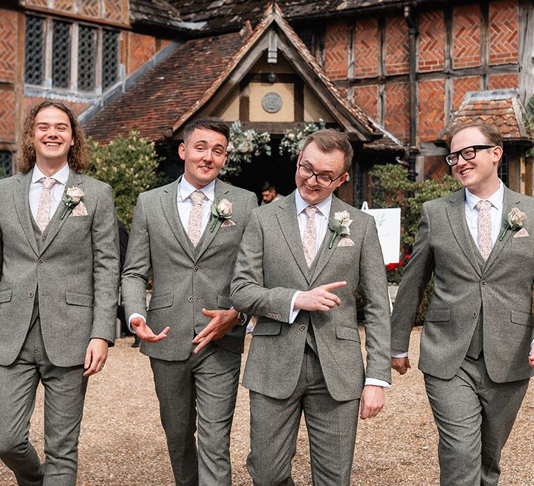 The groom and groomsmen walking together wearing grey suits 