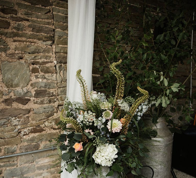 White flowers and foliage inside milk churn with wooden crates and lanterns for wedding decor 