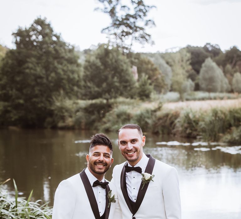 Stunning couple portrait of two grooms wearing white wedding tuxedo suit jackets with white rose buttonholes 