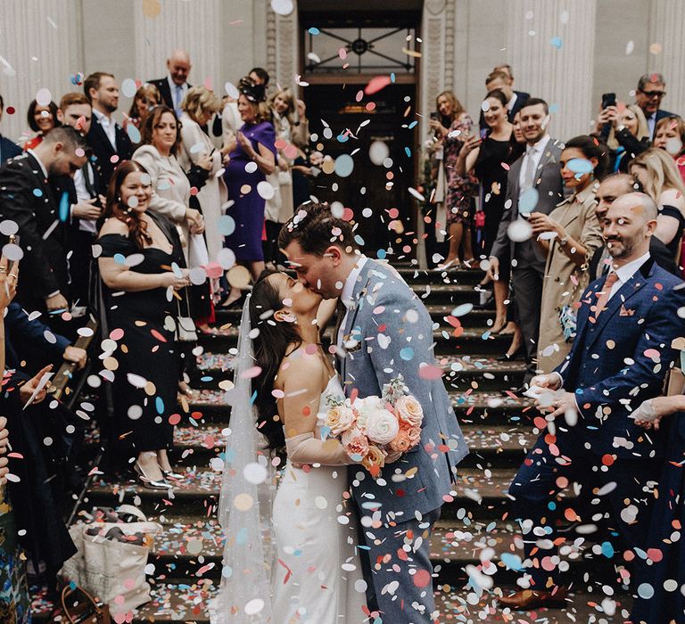 The bride and groom share a kiss as the confetti is thrown over them