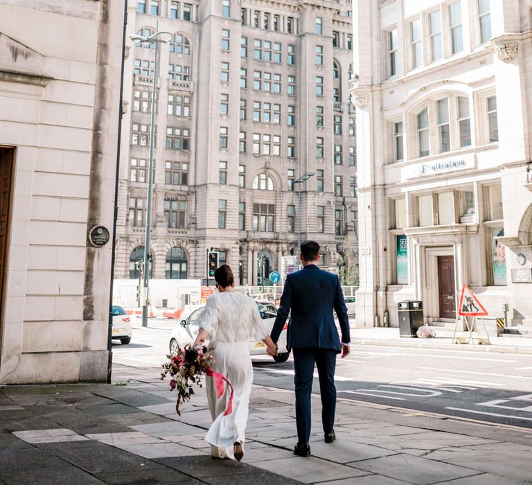 Bride in trouser suit and faux fur cover up walking through Liverpool 