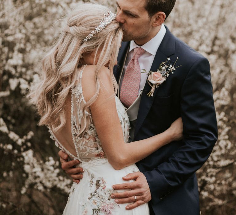 Groom in navy suit and grey waistcoat kissing his brides forehead