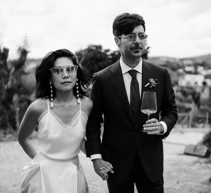 Black and white portrait of stylish bride and groom in shades holding hands 