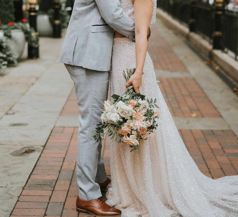 Groom in a light grey suit kissing his brides neck in a sparkly dress outside The Landmark London hotel 