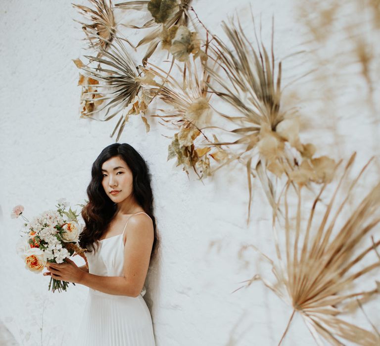 Asian bride wearing a pleated wedding dress to match the dried flower arch