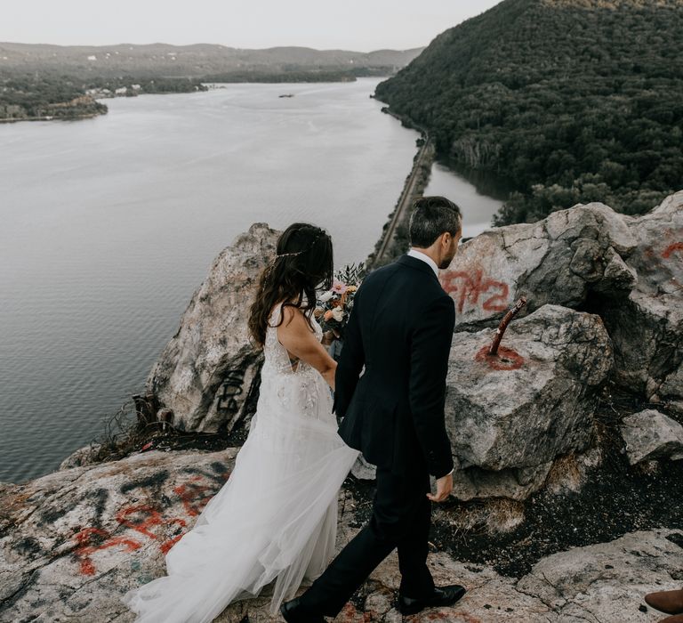 Bride & groom walk along the Hudson River surrounded by rocks