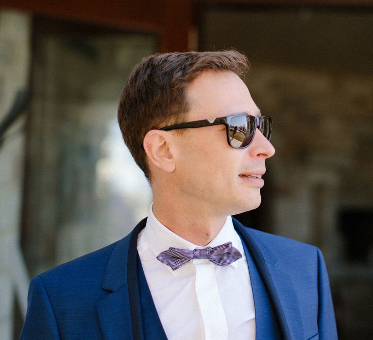 The groom wearing a dark blue three piece suit with a bow tie and sunglasses