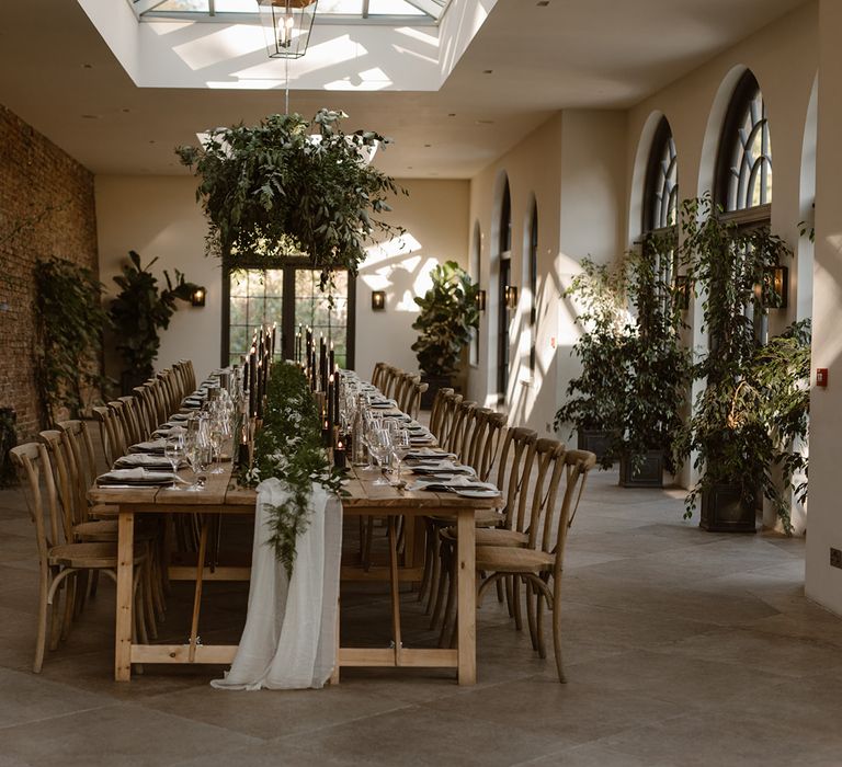 Wooden wedding table with rustic decor, wooden chairs, foliage cloud, greenery and black candles in the Fig House at Middleton Lodge