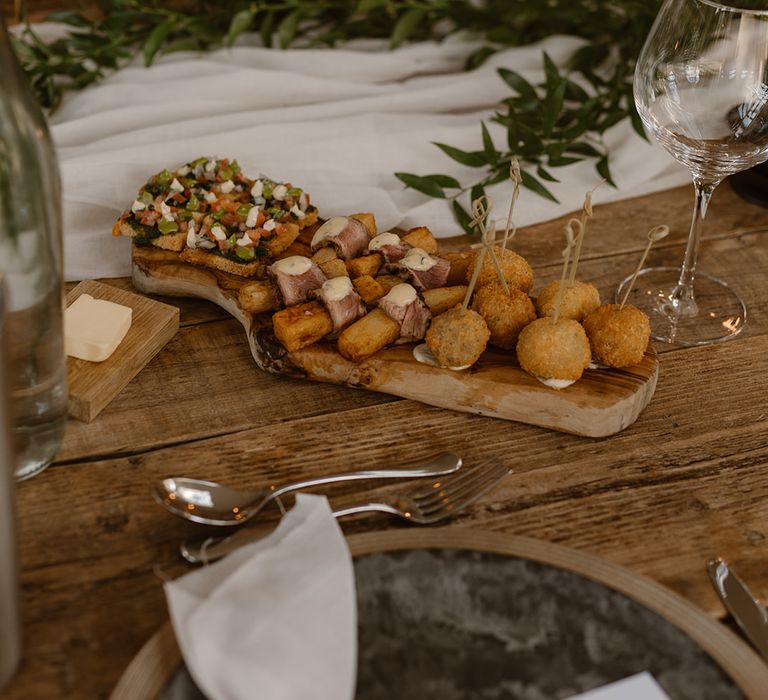 Mediterranean themed platter on wooden board laid at rustic wooden wedding table with, greenery, black candles and tableware