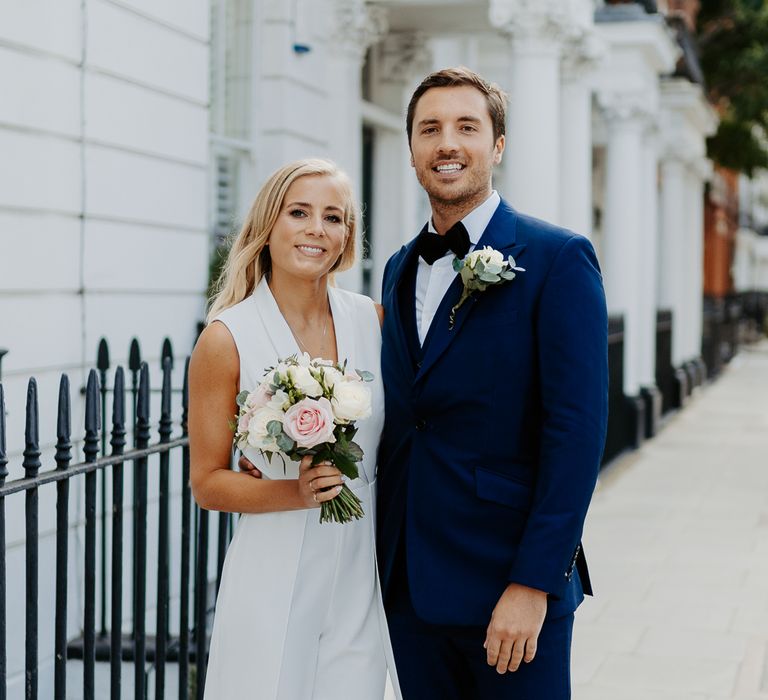 Bride & groom pose together as bride holds white floral bouquet