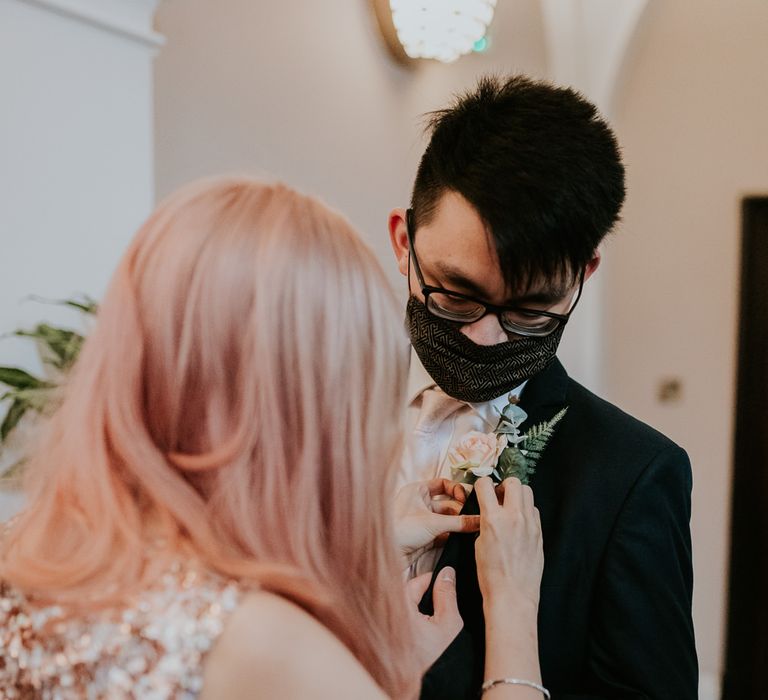 Bride with pink hair putting on the groom buttonhole 