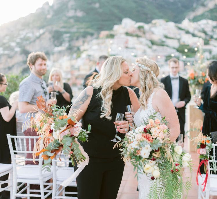 The brides share a kiss as they walk back up the aisle of their outdoor wedding ceremony