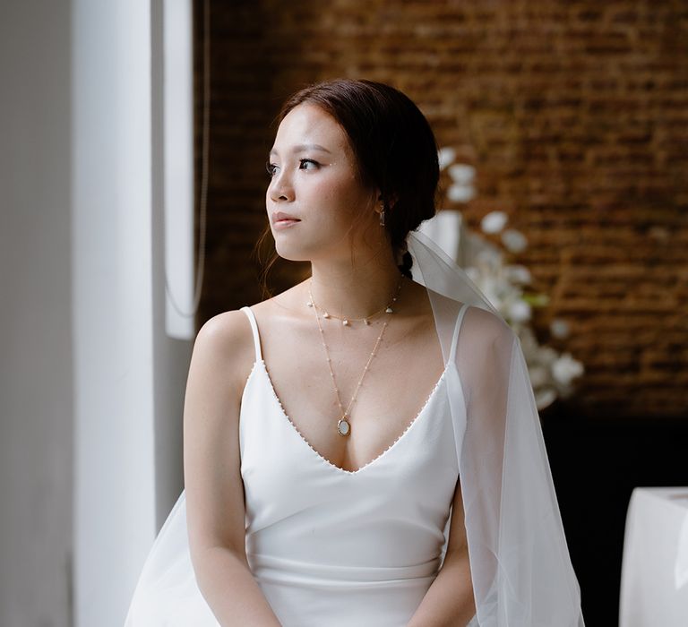 Asian bride in a minimalist wedding dress with gold necklaces and wedding veil 