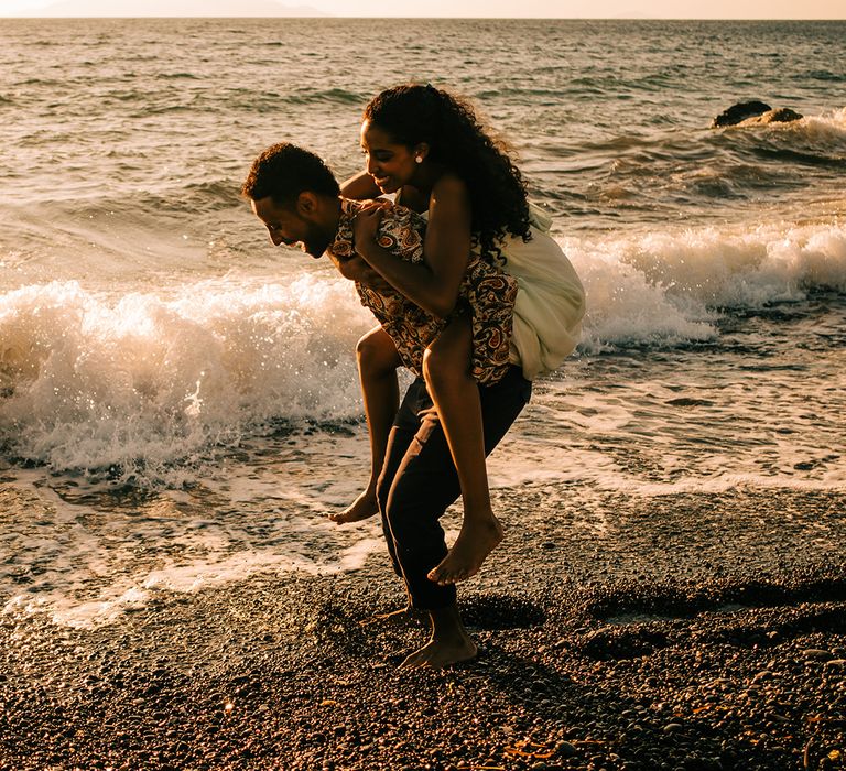 Groom carries bride on his back as they play in the sea