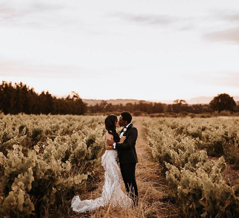 Groom in a tuxedo kissing his bride in a strapless wedding dress in a vineyard in South Africa