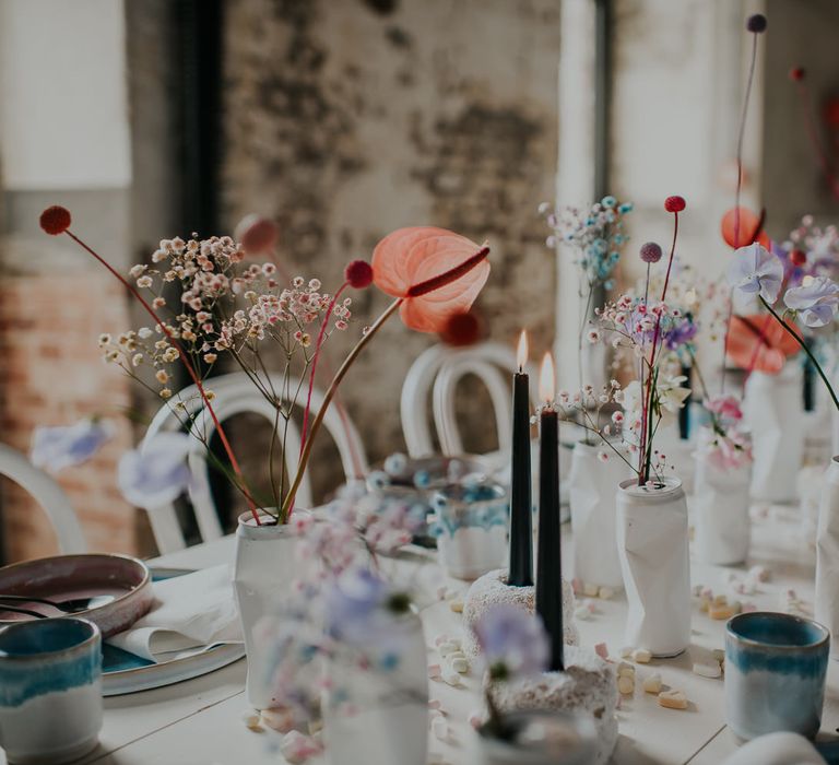 Wedding table decor with white tin cans filled with pastel flowers stems, black taper candles and coloured tableware 