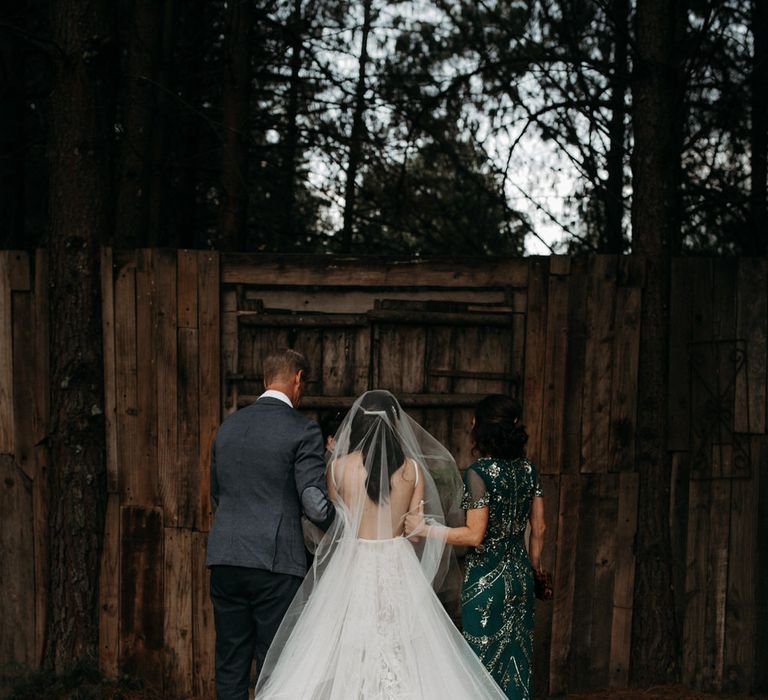 Bride and her parents waiting to enter the ceremony. She is wearing a long tulle veil and layered tulle and applique wedding dress